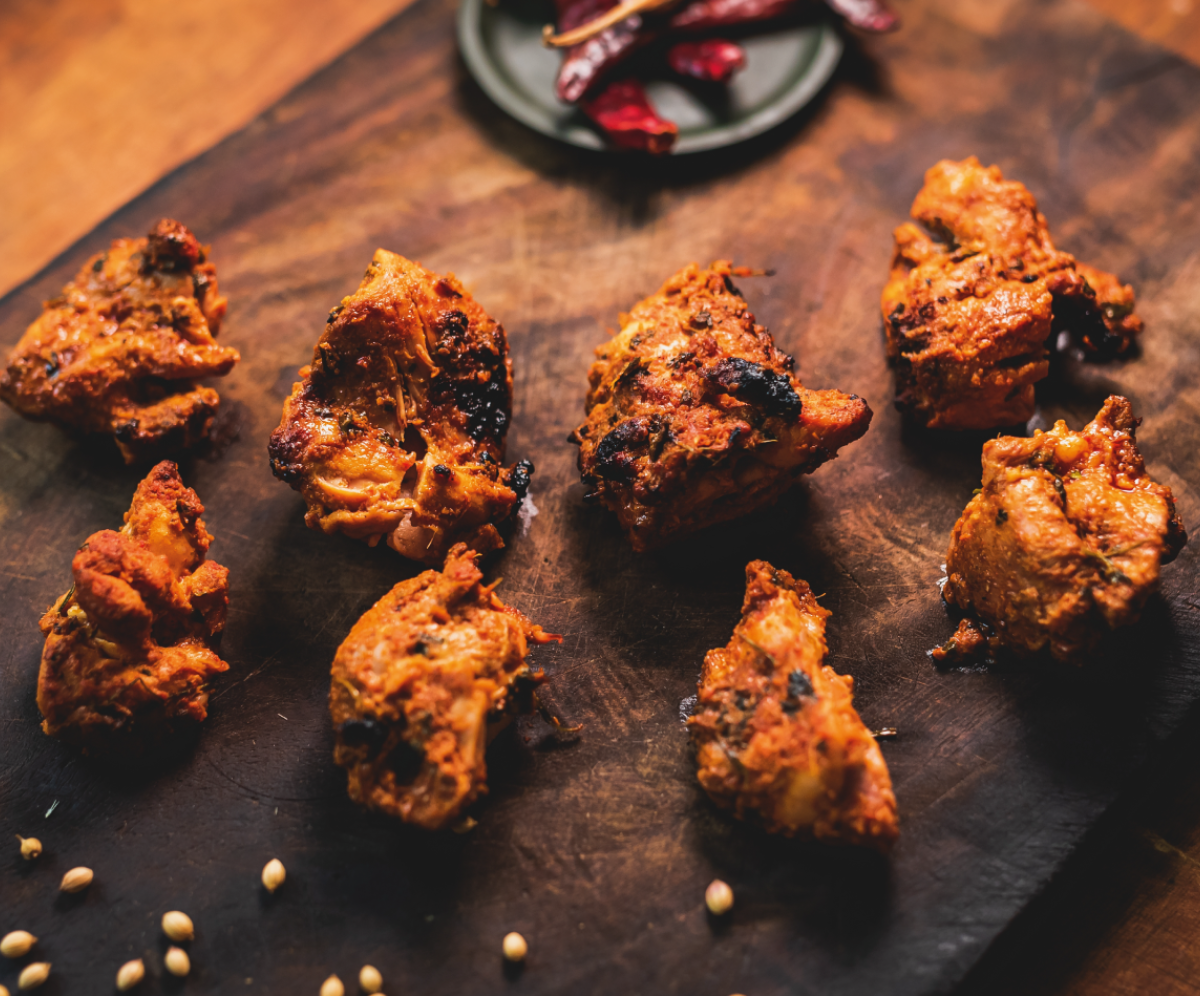 Cooked chicken marinated in spices laying on a wooden board, garnished with dried chilli