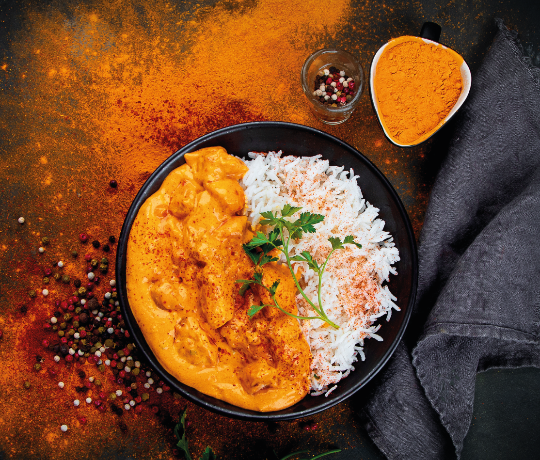 Chicken curry and rice in a black bowl with turmeric splashed on the table underneath